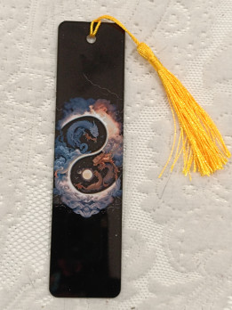 Marque-page noir illustré de deux dragons formant un yin et yang avec un pompon jaune