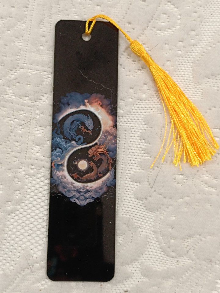 Marque-page noir illustré de deux dragons formant un yin et yang avec un pompon jaune