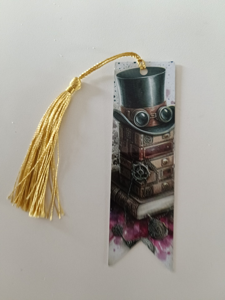 Marque-page illustré d'un haut-de-forme steampunk posé sur des livres avec un pompon doré