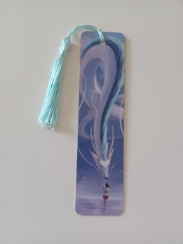 Marque-page illustré d'un grand dragon blanc et bleu avec une fillette et un pompon soyeux bleu clair