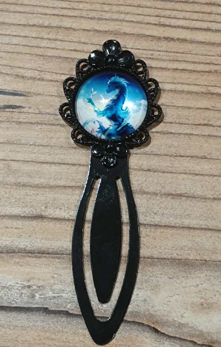 Marque-page noir ouvragé avec cabochon rond illustrant une créature fantastique bleue sur fond céleste