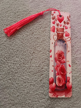 Marque-page illustré d'une fiole avec des roses rouges et des cœurs, orné d'un pompon rose