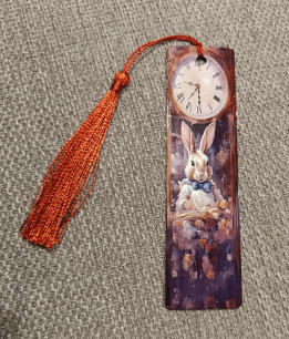 Marque-page illustré d'un lapin habillé lisant un livre sous une horloge ancienne avec pompon roux