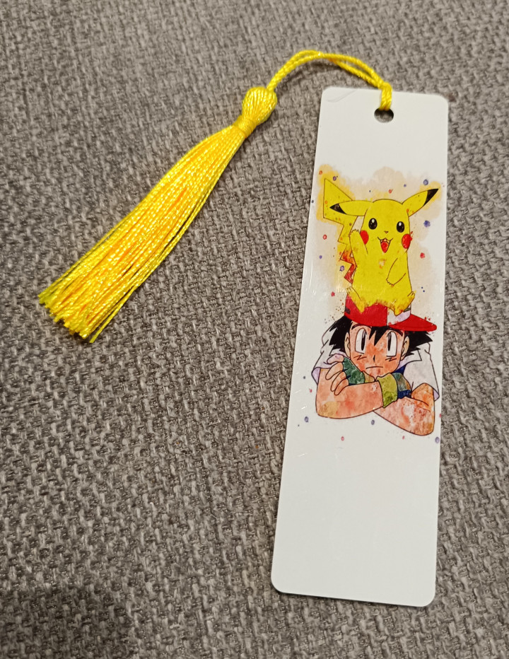 Marque-page blanc illustré d'un garçon à casquette rouge portant une créature jaune sur la tête, avec pompon jaune
