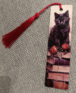Marque-page illustré d'un chat noir assis sur une pile de livres avec roses rouges et pompon
