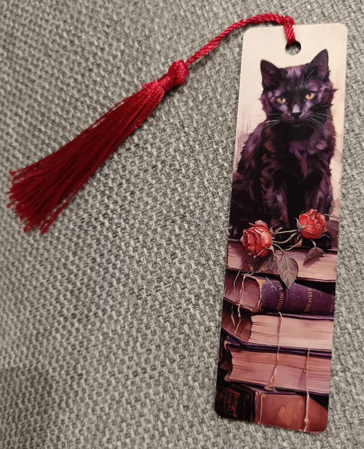 Marque-page illustré d'un chat noir assis sur une pile de livres avec roses rouges et pompon