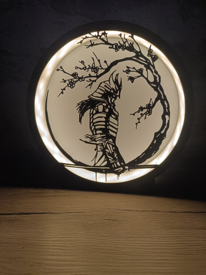 Veilleuse circulaire lumineuse avec silhouette noire de guerrier samouraï sous une branche fleurie