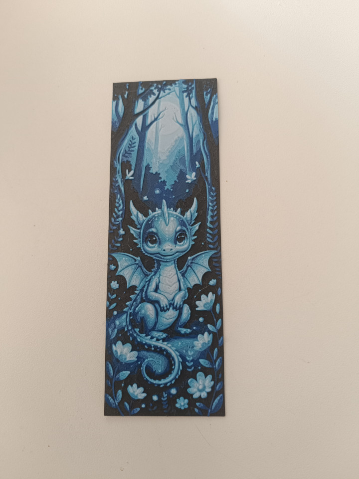 Marque-page en impression 3D illustrant un petit dragon bleu assis dans une forêt aux tons nocturnes