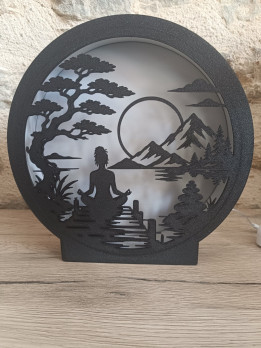 Lampe veilleuse circulaire noire représentant une silhouette en méditation devant un paysage de montagnes et un arbre