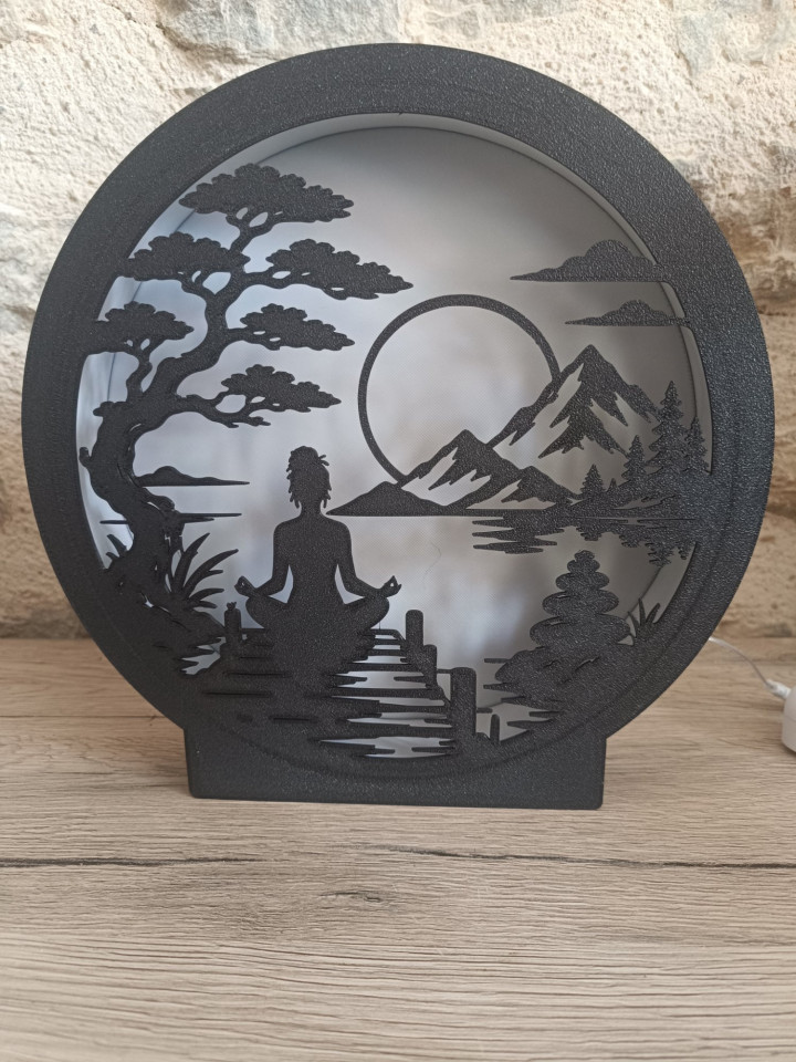 Lampe veilleuse circulaire noire représentant une silhouette en méditation devant un paysage de montagnes et un arbre