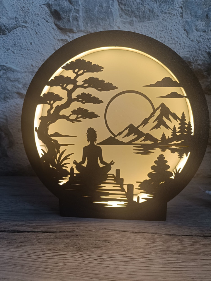 Lampe veilleuse circulaire noire représentant une silhouette en méditation devant un paysage de montagnes et un arbre