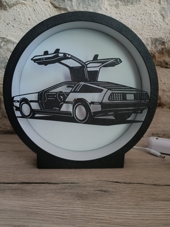 Lampe veilleuse circulaire éclairée avec silhouette noire d'une voiture aux portes papillon ouvertes