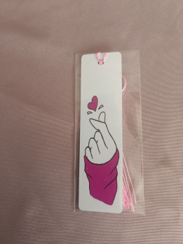 Marque-page blanc en métal avec illustration d'un geste de cœur avec les doigts et pompon rose