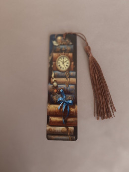 Marque-page en métal illustré d'une pile de livres anciens avec horloge et ruban bleu surmonté d'un pompon marron