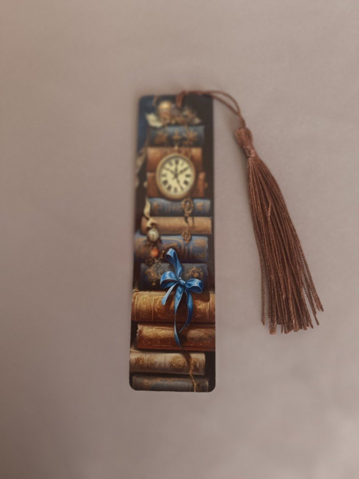 Marque-page en métal illustré d'une pile de livres anciens avec horloge et ruban bleu surmonté d'un pompon marron