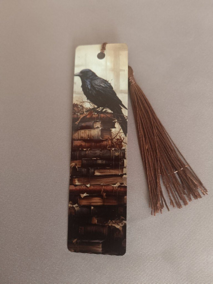 Marque-page en métal illustré d'un corbeau sur une pile de vieux livres avec pompon marron