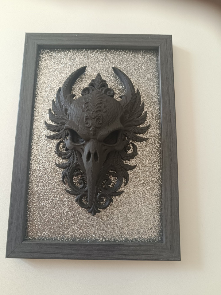 Cadre noir avec sculpture en relief 3D d'un crâne d'oiseau ailé sur fond pailleté argenté