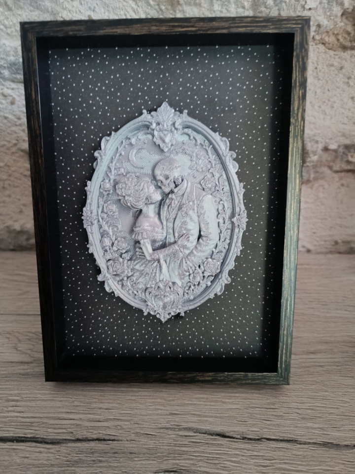 Cadre noir avec médaillon en impression 3D représentant un couple de squelettes enlacés
