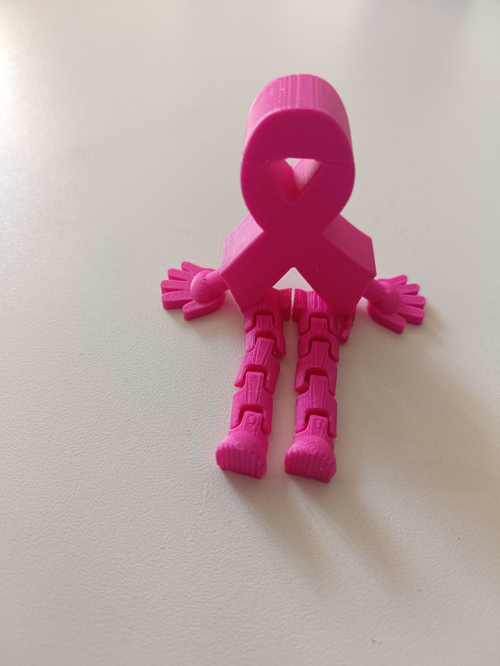 Figurine rose en forme de ruban avec bras et jambes articulées posée sur une table