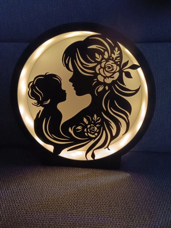 Veilleuse circulaire noire rétroéclairée par LED montrant la silhouette d'une mère et son enfant