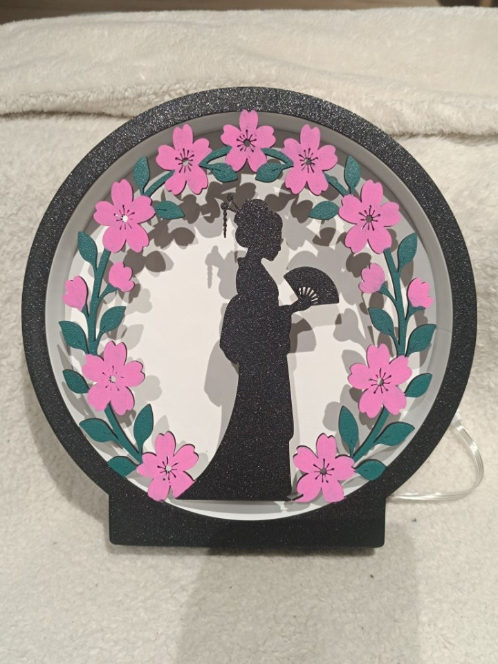 Veilleuse ronde lumineuse avec silhouette noire tenant un éventail et couronne de fleurs roses