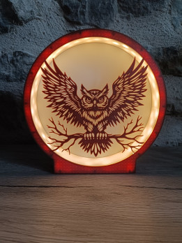 Veilleuse ronde allumée avec silhouette de hibou aux ailes déployées sur une branche