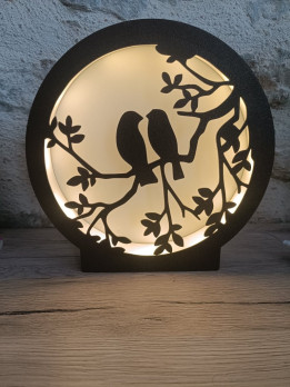 Lampe veilleuse circulaire noire en impression 3D avec silhouette de deux oiseaux sur une branche rétroéclairée