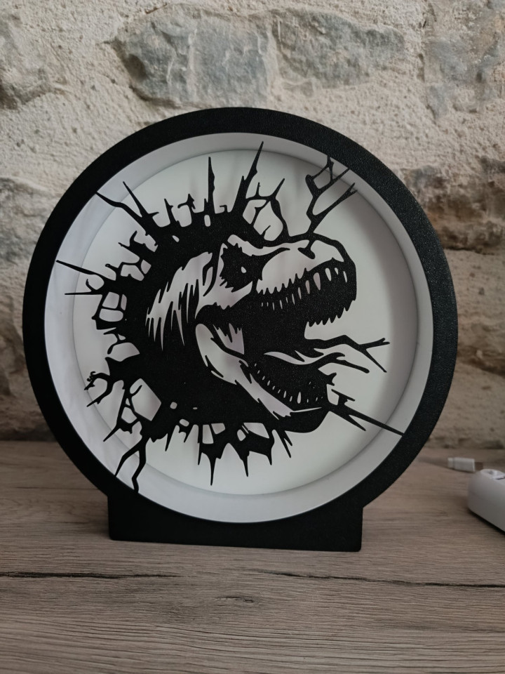 Lampe ronde noire en impression 3D avec éclairage LED et silhouette de dinosaure surgissant d'une brèche