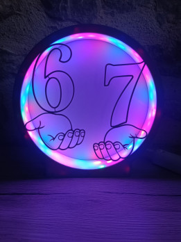 Veilleuse ronde noire illuminée montrant les chiffres 6 et 7 sur des mains stylisées avec contour LED rose et bleu