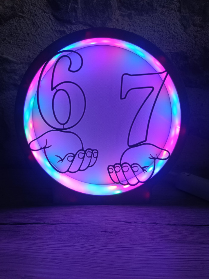 Veilleuse ronde noire illuminée montrant les chiffres 6 et 7 sur des mains stylisées avec contour LED rose et bleu