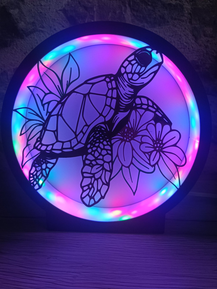 Lampe ronde noire avec silhouette de tortue marine et fleurs éclairée par des LED multicolores