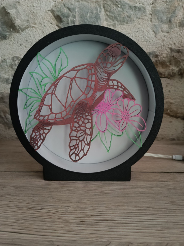 Lampe ronde noire avec silhouette de tortue marine et fleurs éclairée par des LED multicolores