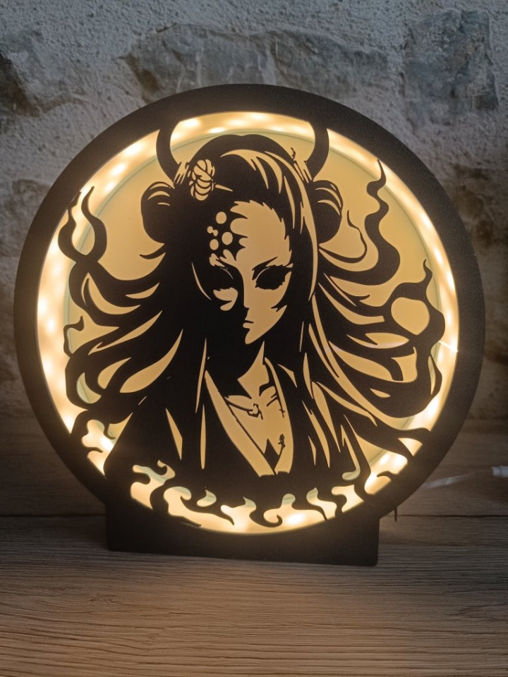 Lampe ronde noire éclairée par des LED chaudes révélant la silhouette découpée d'une femme aux cornes et aux cheveux flamboyants
