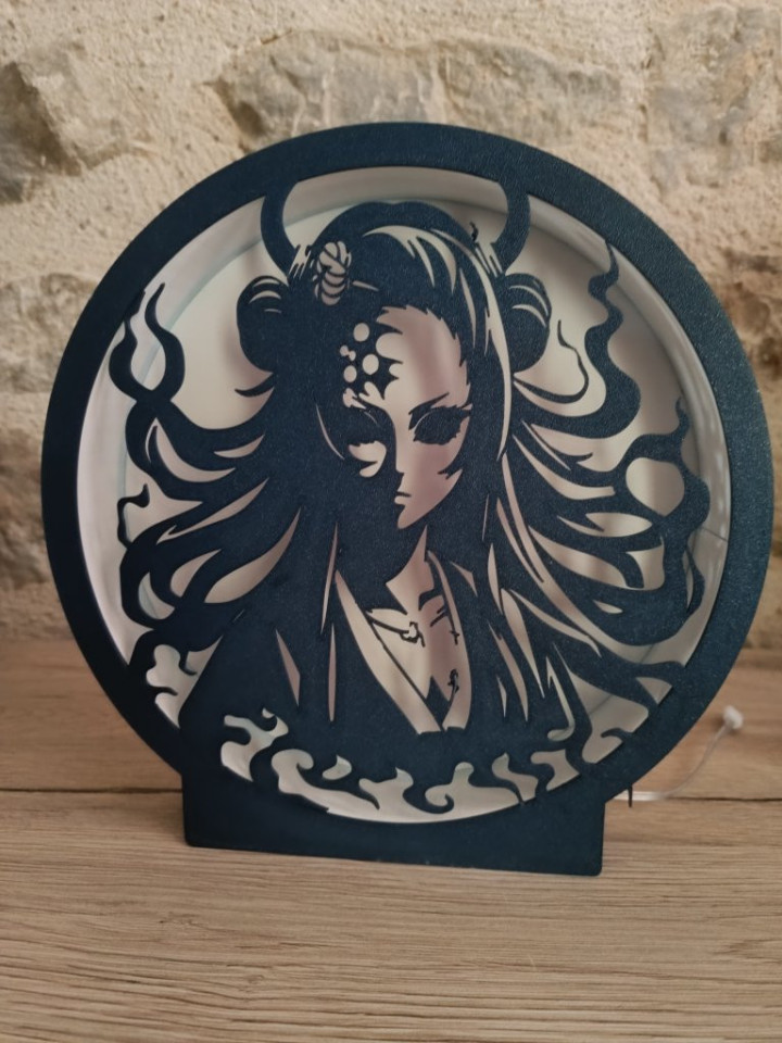 Lampe ronde noire éclairée par des LED chaudes révélant la silhouette découpée d'une femme aux cornes et aux cheveux flamboyants