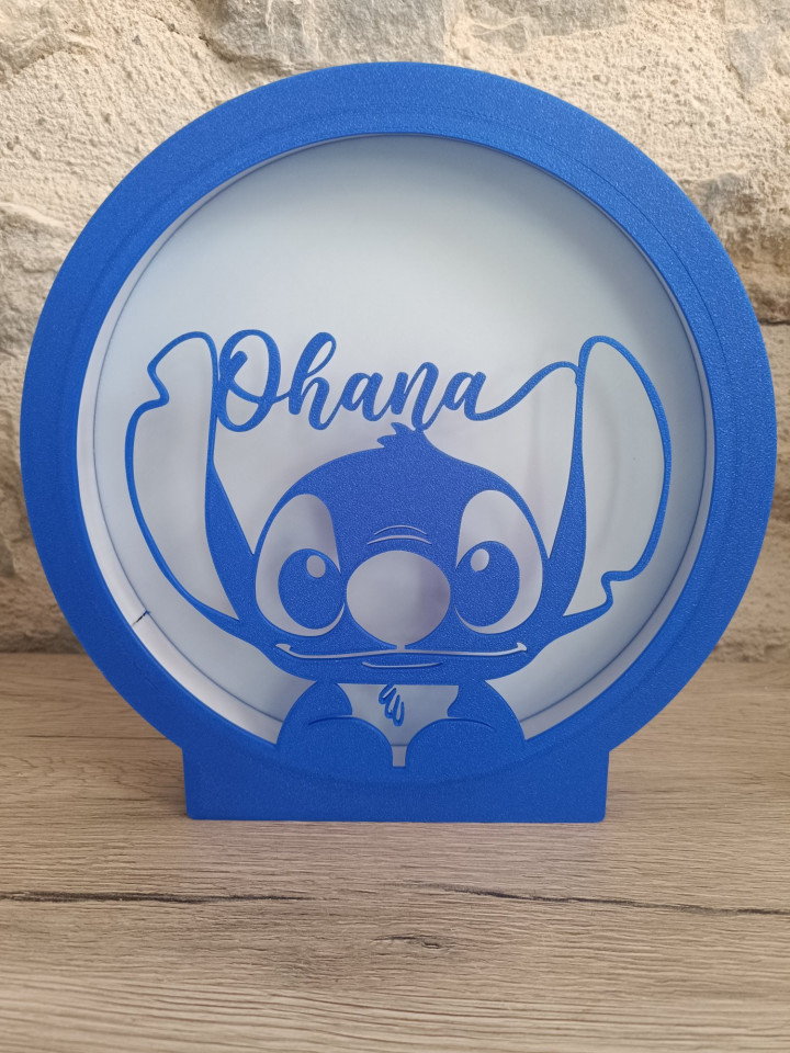 Veilleuse circulaire lumineuse bleue avec silhouette de créature aux grandes oreilles et inscription Ohana