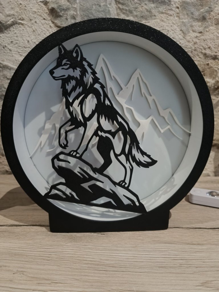 Lampe circulaire avec silhouette de loup sur un rocher et montagnes rétroéclairées par des LED