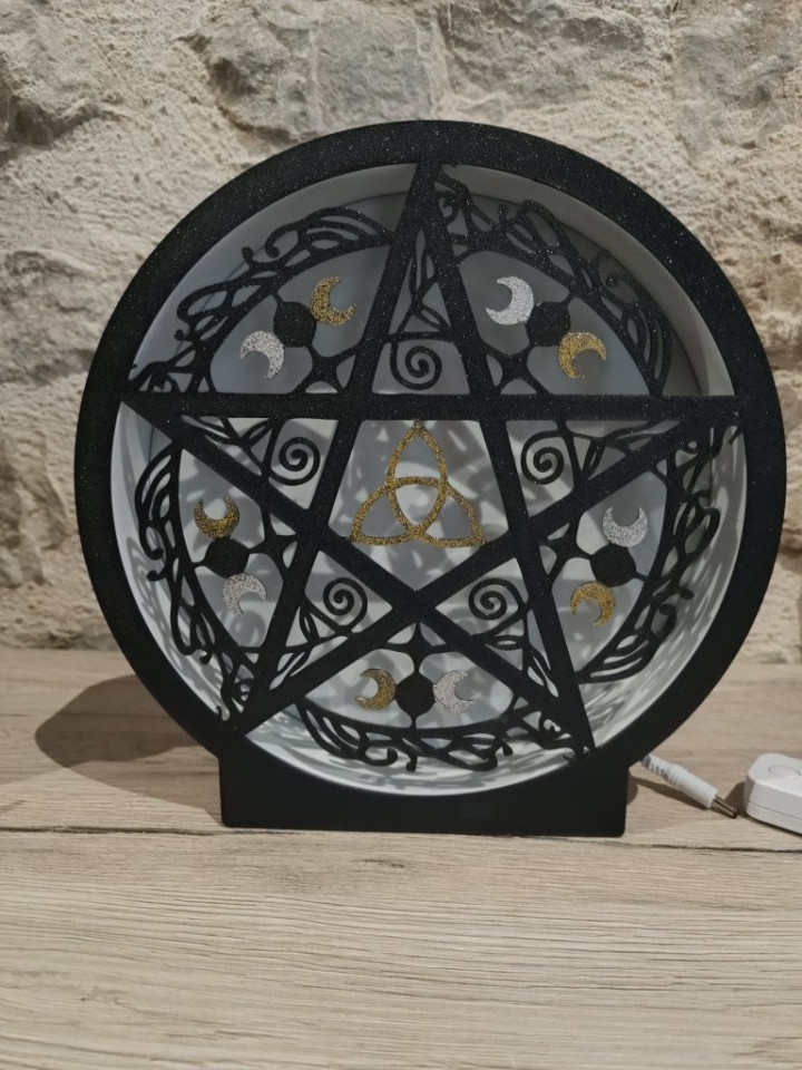 Lampe circulaire noire allumée avec silhouette de pentagramme, triquetra et croissants de lune